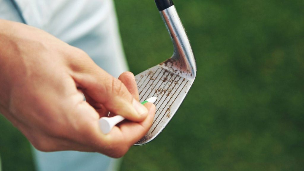 Golfer using a tee to clean dirt from the grooves of an iron club on the course