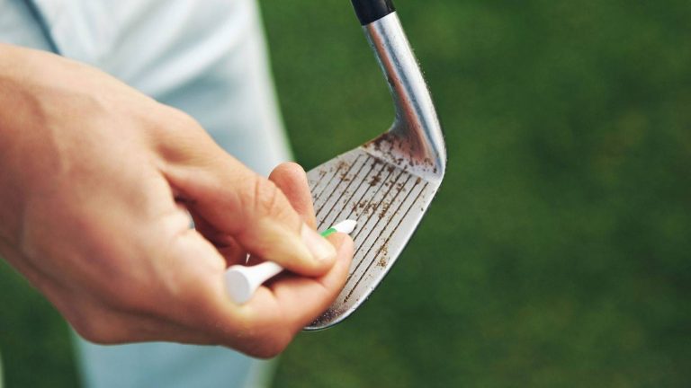 Golfer using a tee to clean dirt from the grooves of an iron club on the course